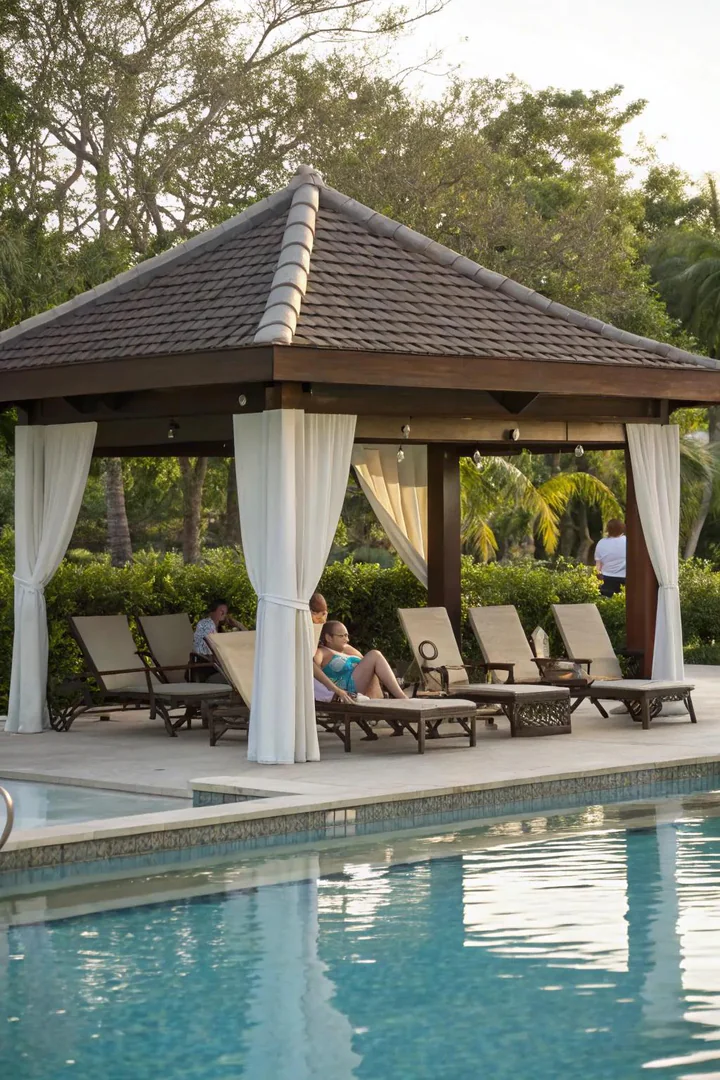 Pavilion beside a swimming pool with lounge chairs and outdoor curtains